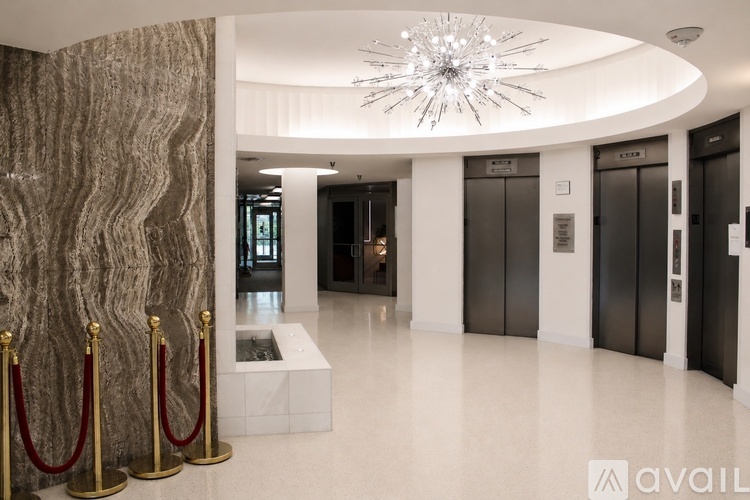 A chandelier hangs from the ceiling in a white hallway with elevators on either side.