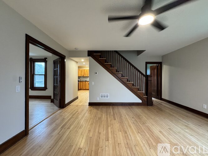 A spacious room with wooden floors and a staircase leading to the upper level.