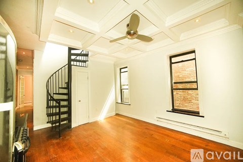 A spacious room with a wooden floor and a window with a brick wall view.