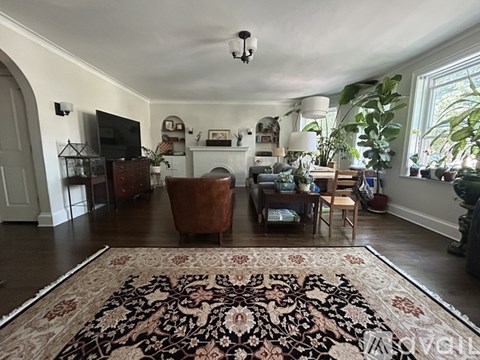 A living room with a rug on the floor and a TV on the wall.