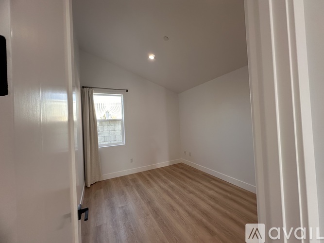 A room with wooden flooring and white walls, with a window and a door visible.