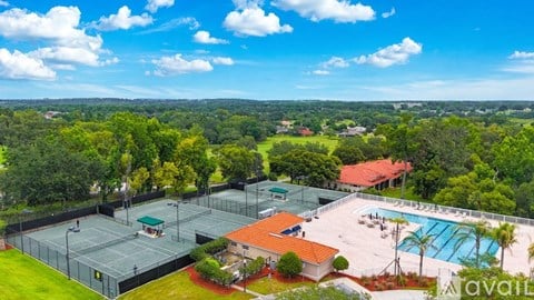 A tennis court surrounded by a fence with a pool and a house in the background.