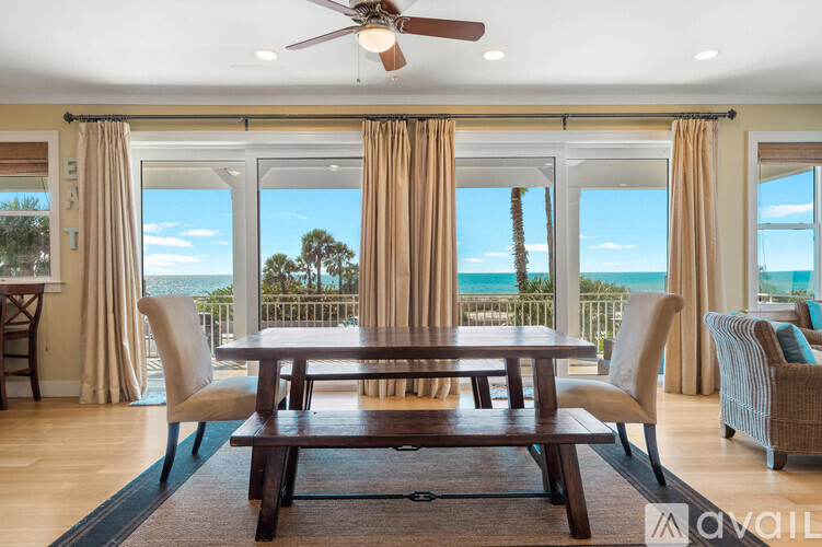 A dining room with a table and chairs in front of a large window with a view of the ocean.