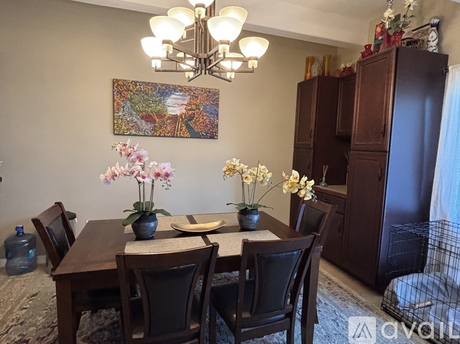 A dining room with a wooden table and chairs, a chandelier, and a painting on the wall.