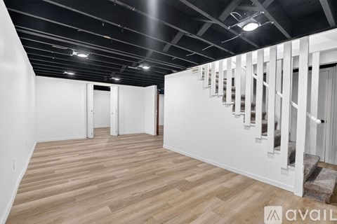 A spacious room with wooden flooring and a staircase on the right side.