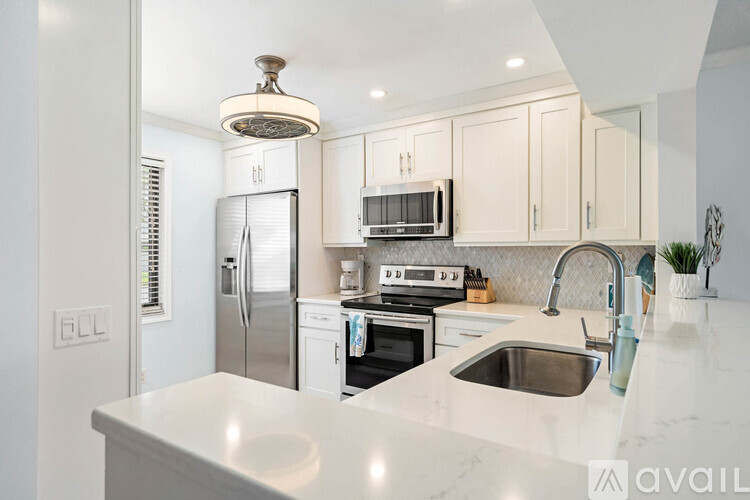 A kitchen with white cabinets and appliances, a marble countertop, and a person standing by the sink.