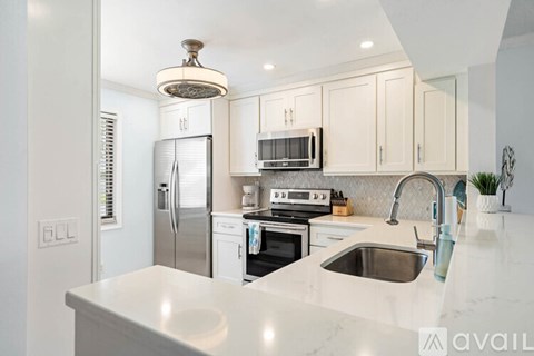 A kitchen with white cabinets and appliances, a marble countertop, and a person standing by the sink.