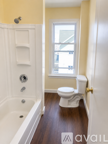 A white bathtub with a window above the toilet in a bathroom.