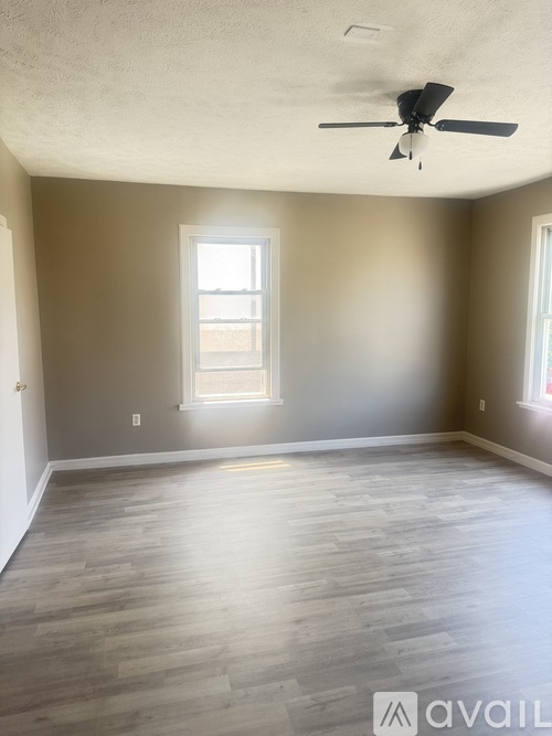 A room with a ceiling fan and light, hardwood floors, and a window letting in natural light.
