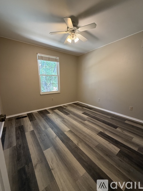 A room with a ceiling fan and a window with a view of trees.