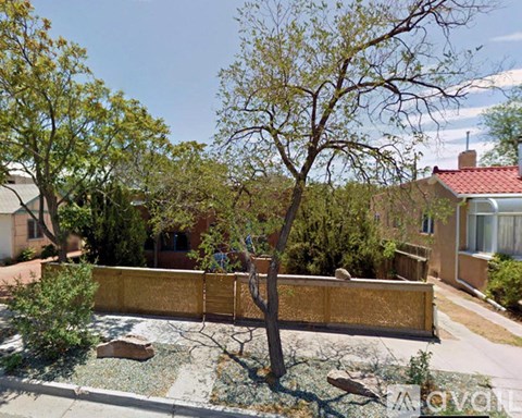 A tree in a yard with a fence and houses in the background.