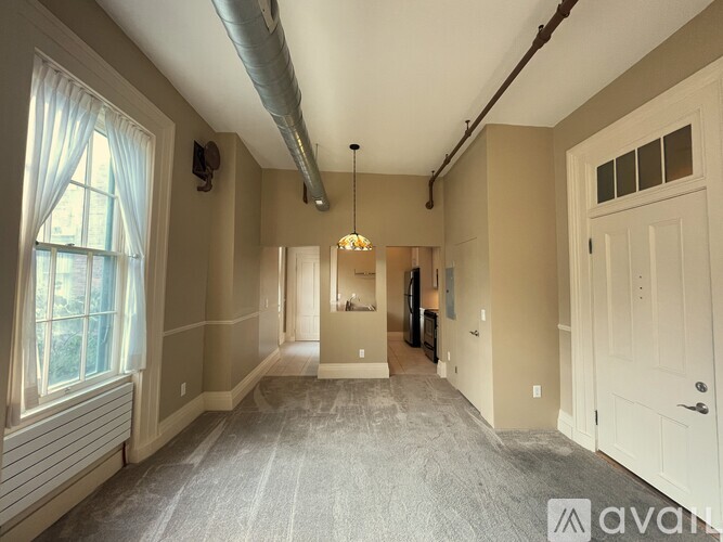 A spacious room with a carpeted floor and a large window on the left side.