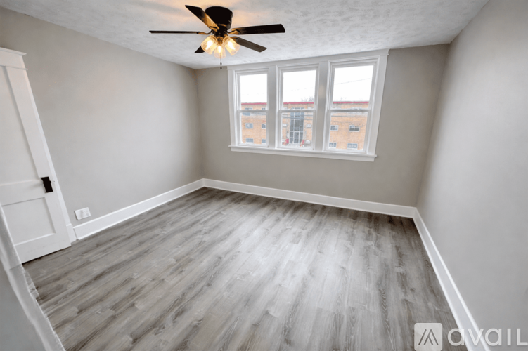 A room with a ceiling fan and a window overlooking a building.