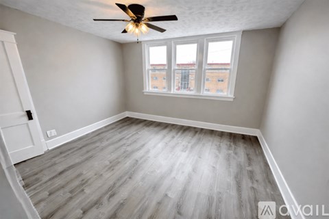 A room with a ceiling fan and a window overlooking a building.