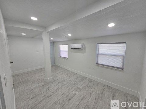 A spacious room with a door, window, and a wall-mounted air conditioner unit.