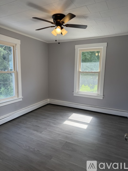 A room with a ceiling fan and two windows.