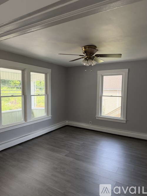 A room with a ceiling fan and two windows.