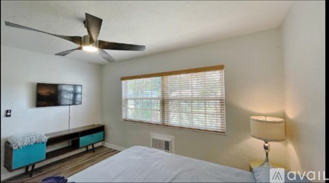 A bedroom with a bed, a television, a window with blinds, a ceiling fan, and a lamp.