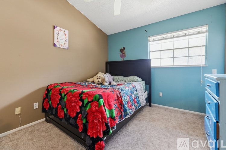 A bedroom with a bed covered in a red floral comforter and a teddy bear on the bed.