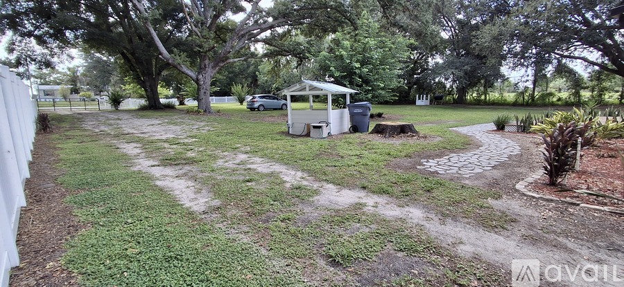 A backyard with a white fence, a gazebo, and a gravel path.