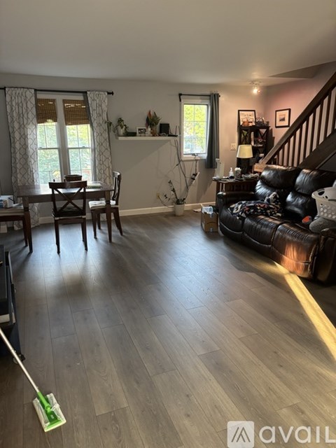 A living room with a black leather couch and wooden floors.