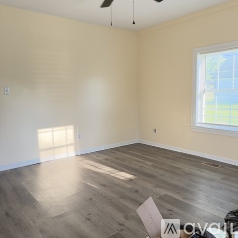 A room with wooden flooring and a window letting in sunlight.
