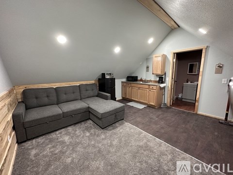 A living room with a grey sofa and a kitchen area in the background.
