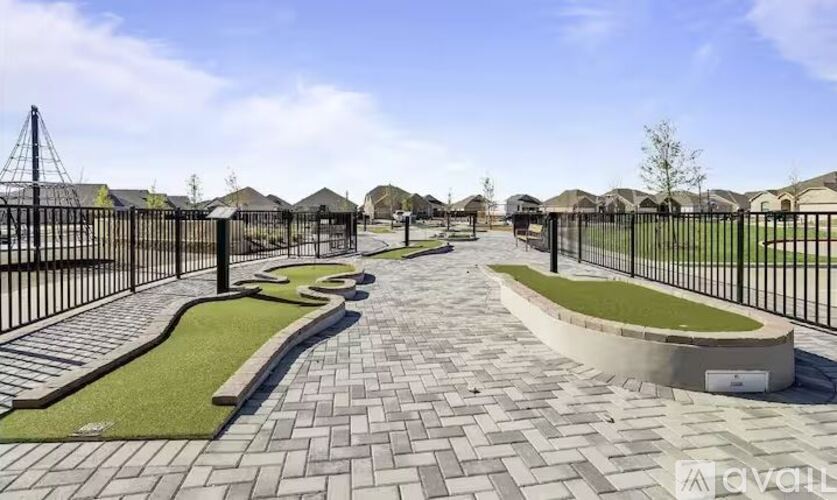 A paved walkway with grassy areas and a metal fence leads to a row of houses.