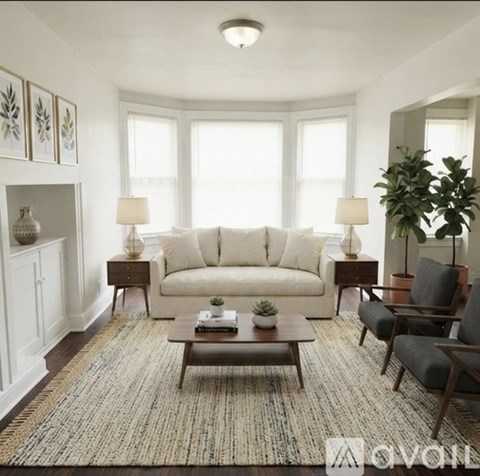 A living room with a white sofa, a wooden coffee table, and a large rug.