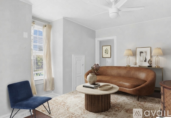 A living room with a brown leather sofa, a blue chair, and a coffee table with a vase and a book on it.