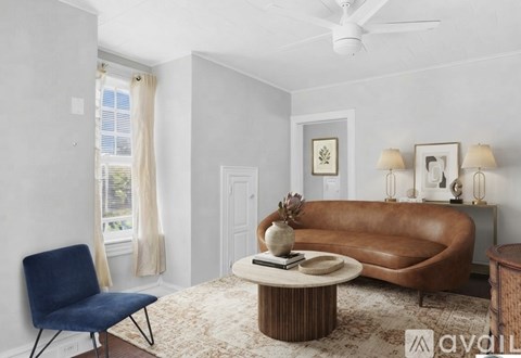 A living room with a brown leather sofa, a blue chair, and a coffee table with a vase and a book on it.