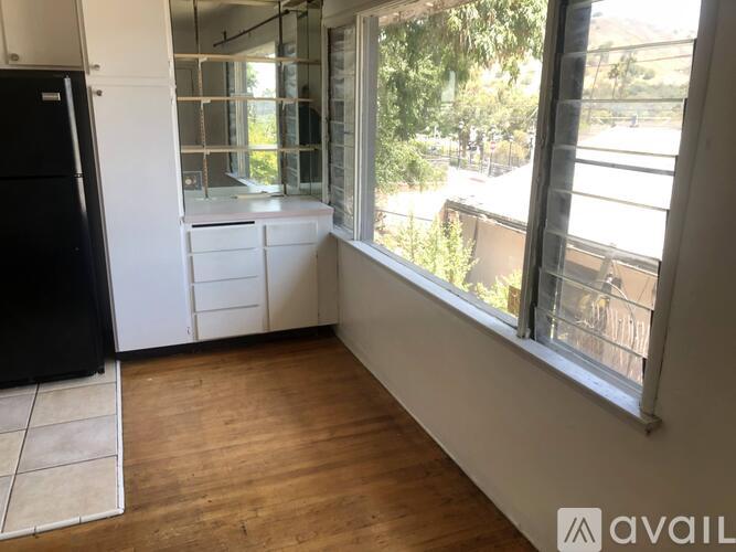A kitchen with a black fridge, white cabinets, and a wooden floor.