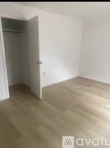 A room with a wooden floor and white walls, with a door open to another room.