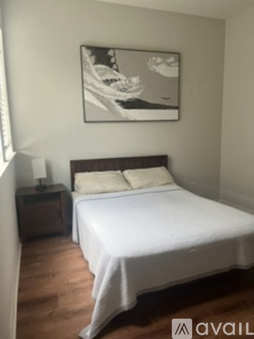 A bedroom with a bed, nightstand, and a picture on the wall.