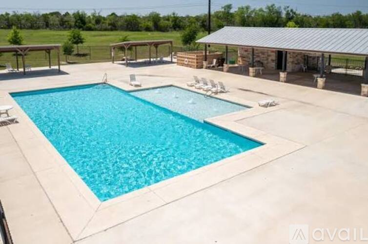 A large outdoor swimming pool surrounded by a concrete patio and a covered area.