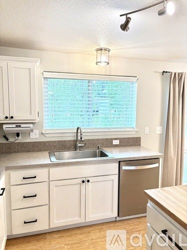 A kitchen with white cabinets and a window with blinds.