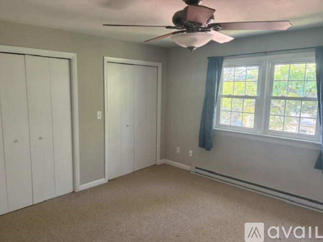 A room with a ceiling fan and a window with a view of trees outside.