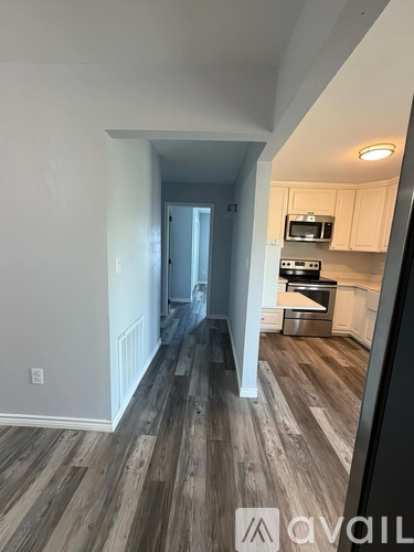A hallway with wood flooring leads to a kitchen area.