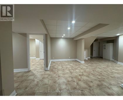 A spacious room with beige carpeting and white walls, with a logo for REALTOR® in the top left corner.