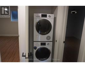A tall front loading washing machine with a dryer on top is in a room with wooden floors.