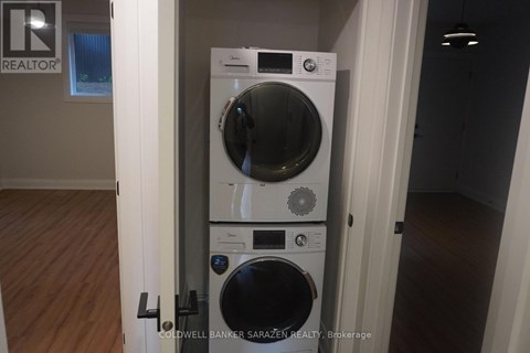 A tall front loading washing machine with a dryer on top is in a room with wooden floors.