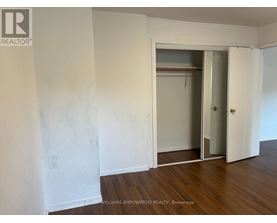 A room with a white wall and a wooden floor with a door and a closet.