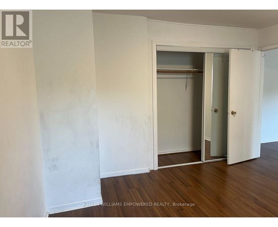 A room with a white wall and a wooden floor with a door and a closet.