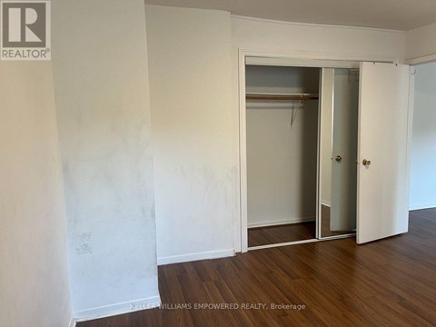 A room with a white wall and a wooden floor with a door and a closet.