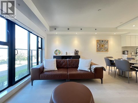 A brown leather sofa with white pillows sits in a modern living room with a dining table and chairs.