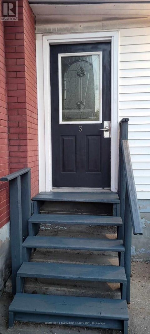 A black door with a glass window is on a red brick wall.
