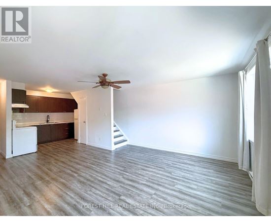A spacious room with a ceiling fan and a staircase leading to another room.