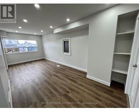 A room with wooden flooring and white walls, with a window and a door visible.