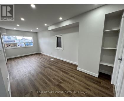 A room with wooden flooring and white walls, with a window and a door visible.