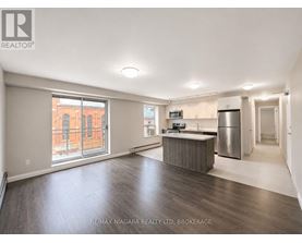 A spacious, empty room with a kitchenette and a refrigerator.